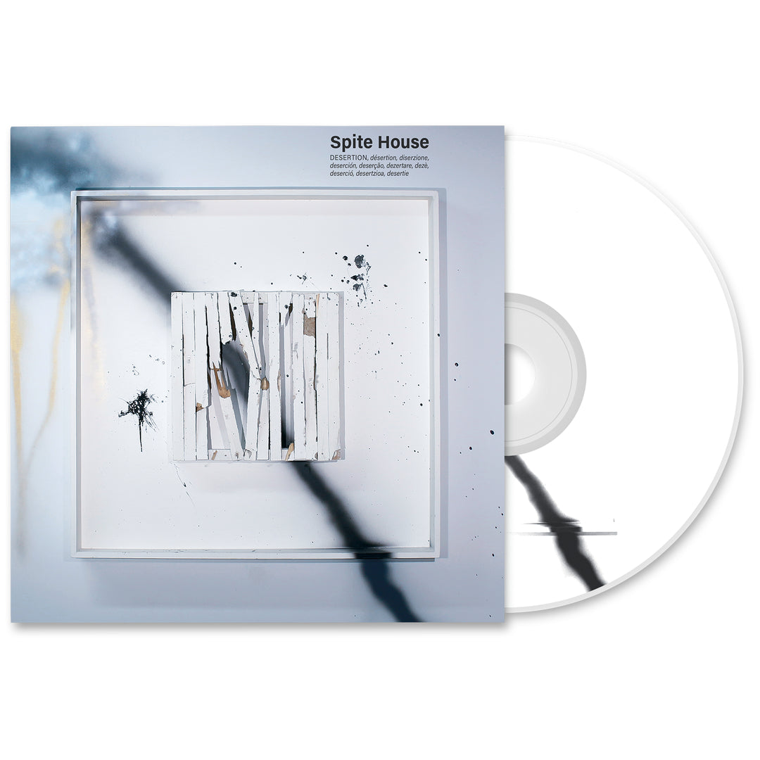 A white Desertion CD slips from its square case. The cover art shows abstract vertical white wooden planks, black streaks, paint splatters, and the Spite House brand name with the tracklist at the top.
