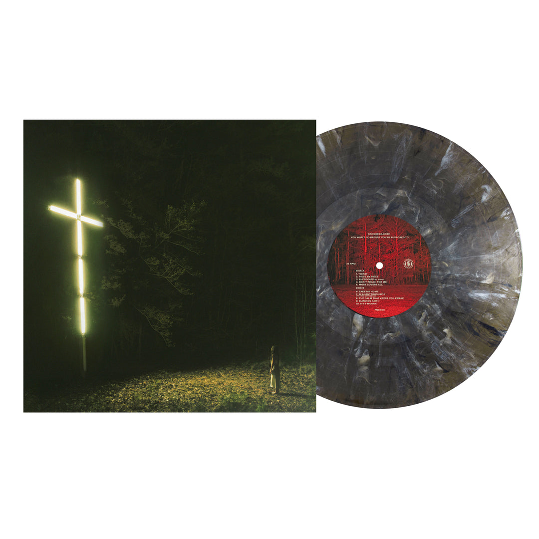 A Knocked Loose Onyx 3rd Press vinyl with a marbled black and gray pattern sits next to its album cover, which features a glowing cross in a dark forest and a small figure standing beneath it.