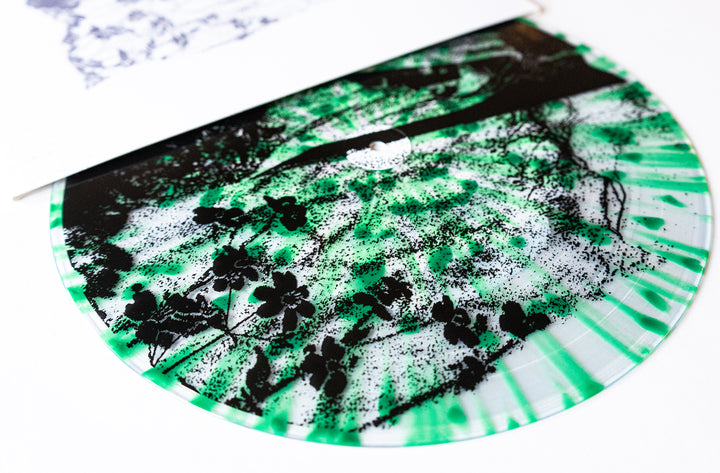 A close-up of a Ben Quad vinyl record with green, black, and white marbled patterns plus black flower silhouettes, partially pulled from a white sleeve; includes pressing info for collectors.