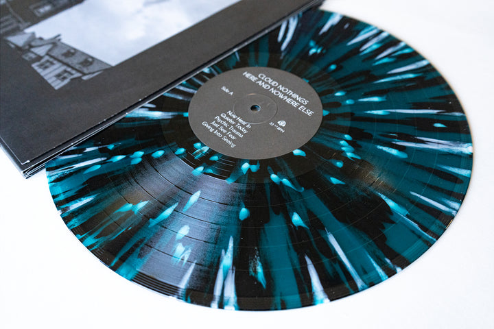 A teal and black splatter vinyl for Here and Nowhere Else by Cloud Nothings is partially out of its sleeve, showing the label—available now for presale.