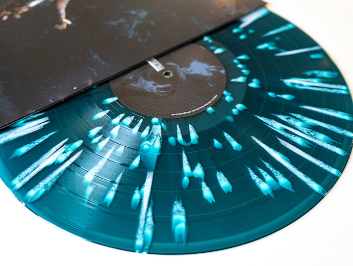 A close-up of The Amity Afflictions royal blue vinyl with teal marbling and white splatter, partially slid from its black cover—an exclusive September 2024 release with the Redux tracklist.