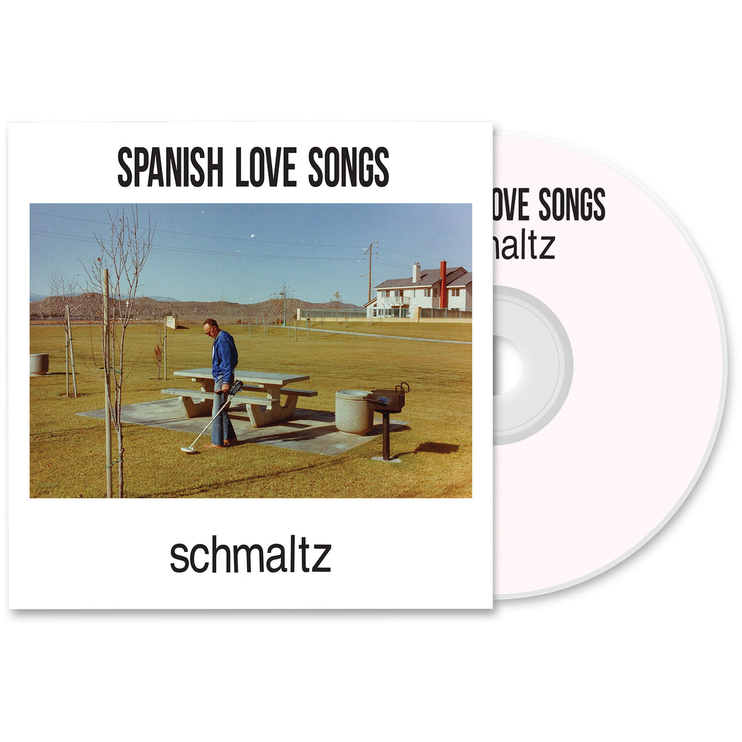 A Spanish Love Songs Schmaltz CD and cover from the album presale bundle. The cover shows a person in a blue jacket by a picnic table in an empty park with grass, trees, and distant buildings under a clear sky.