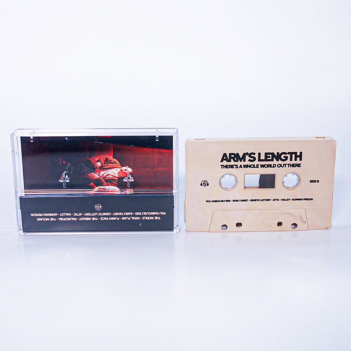 A beige cassette tape labeled Arms Length: Themes & Whole World Out There sits next to its clear case, displaying cover art of a person on a red couch in a dim room—an exciting presale from Arms Length before the album drops.
