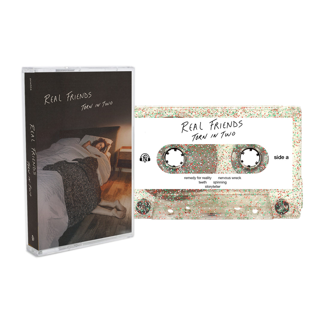 A Clear Glitter Cassette labeled Torn in Two by Real Friends sits next to its case, which shows a person lying in bed under a blanket in a dim room. Includes full album digital download.