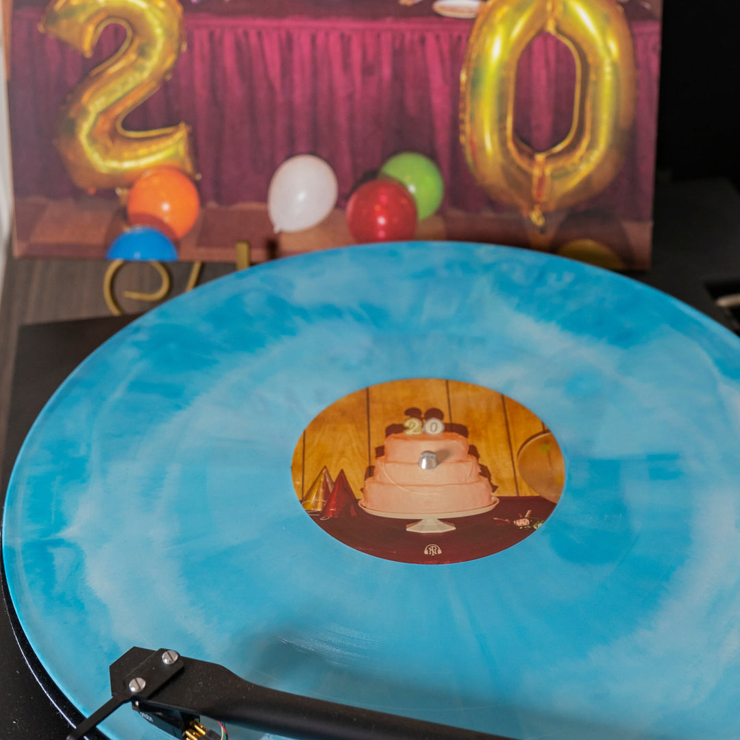 A blue marbled presale vinyl by The Early November spins on a turntable. Its label shows a pink cake with 20 candles, party hats, and balloons, echoing the festive birthday decor and gold “20” balloons in the background.