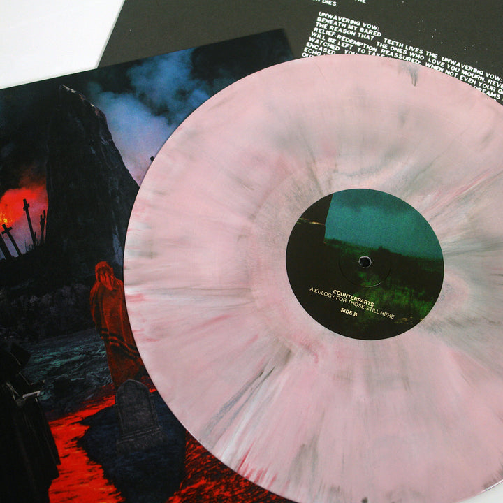 A pink, gray, and oxblood marbled vinyl record by Counterparts rests on a dark album cover with a red-cloaked figure and rocky landscape beneath a stormy sky. Part of a lyric sheet appears in the background.