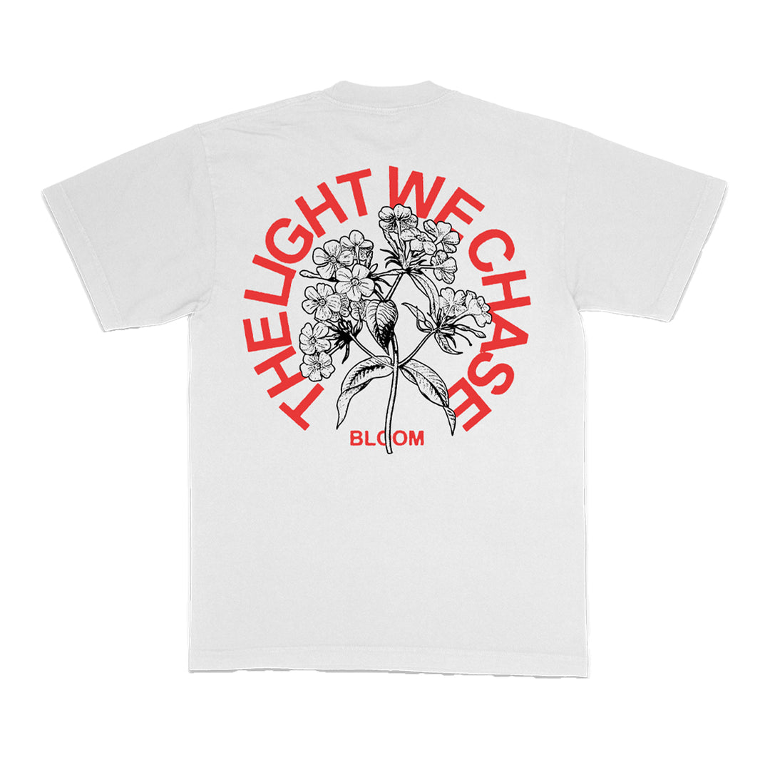 The Bloom white T-shirt showcases a bold black floral illustration on the back, with red arched text reading THE LIGHT WE CHASE and BLOOM printed in red below the design.