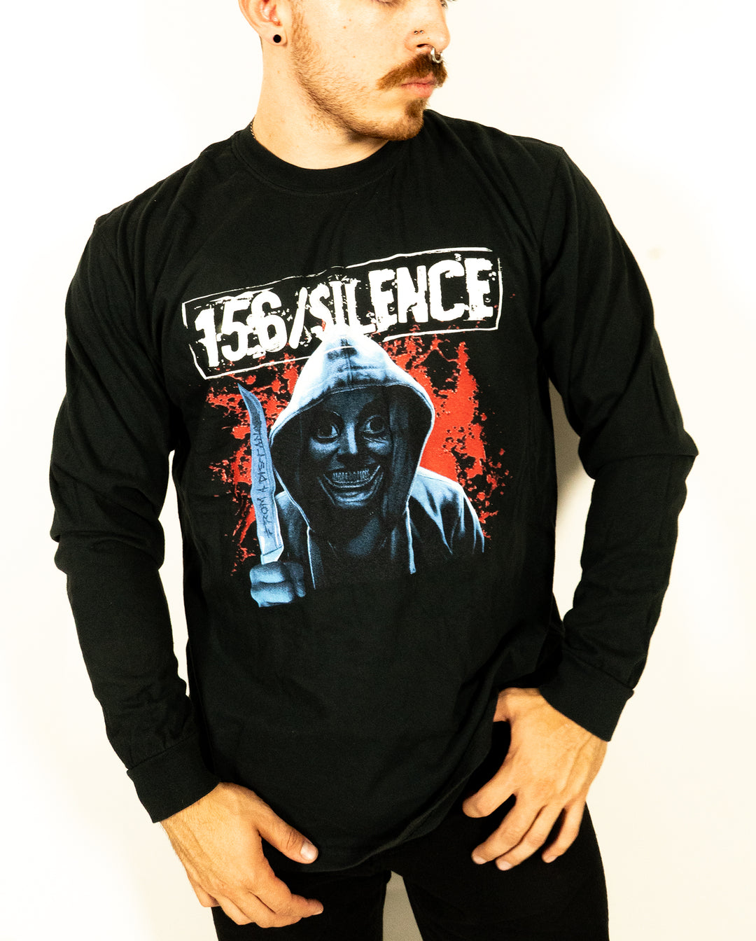 Man in a black Comfort Colors long sleeve shirt featuring a hooded figure holding a knife, with 156/Silence text above and a red splatter background on the shirt’s graphic. Crafted from soft ring spun cotton and garment dyed for added comfort.
