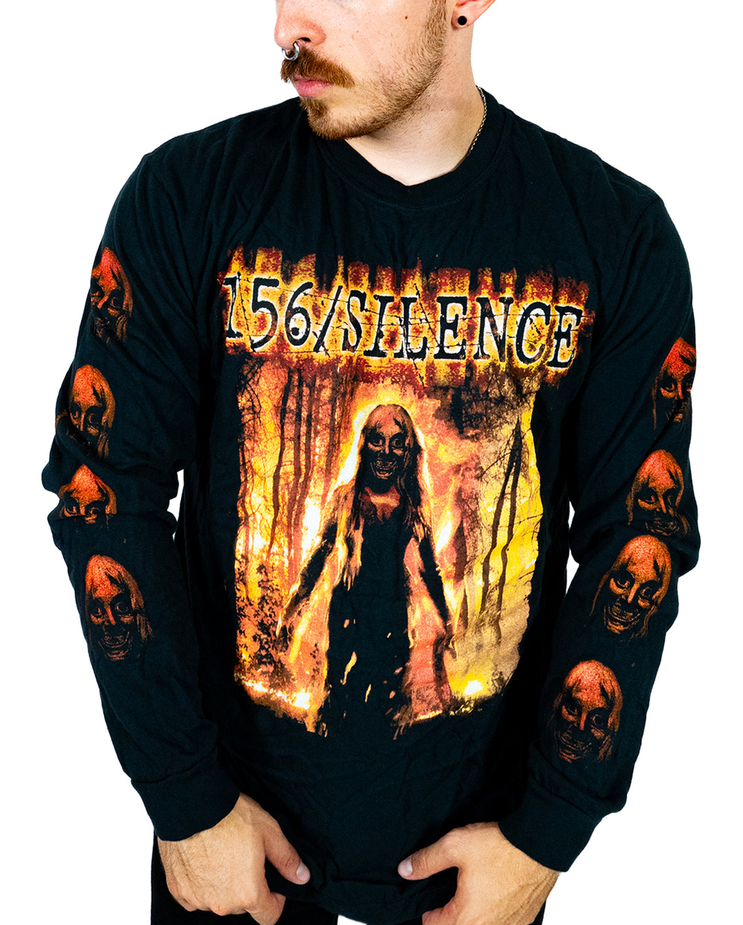 A person wearing a black Comfort Colors long sleeve shirt with 156/SILENCE and a horror-themed graphic of a figure in flames. Made from soft ring spun cotton and garment dyed for lasting quality, the sleeves feature multiple red skulls. The person is looking to the side.