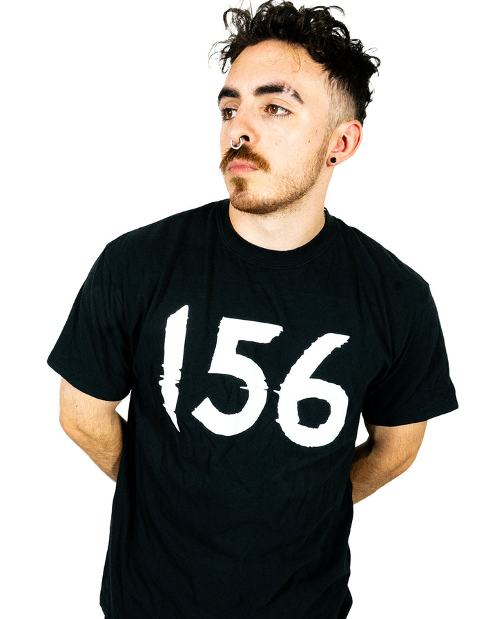A person with dark curly hair, facial hair, and piercings wears a black Comfort Colors T-Shirt made from soft ring-spun cotton with the number 156 in bold white print, standing against a plain white background.