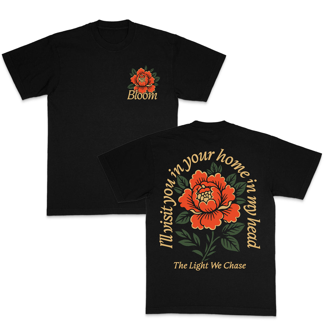 The Bloom black t-shirt features a red-orange flower with green leaves and Bloom text on the front left chest; on the back, a large flower appears with Home Is In My Head; in my head. The Light We Chase. A standout piece from Bloom.