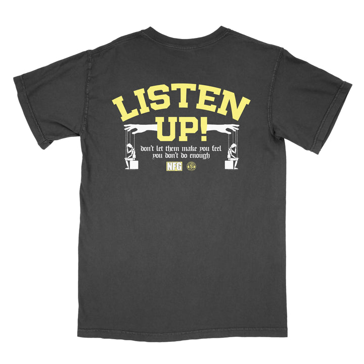 A black New Found Glory tee with bold yellow "Listen Up!" text on the back, smaller text "don’t let them make you feel you don’t do enough," and two illustrated arms holding wireless audio microphones below.