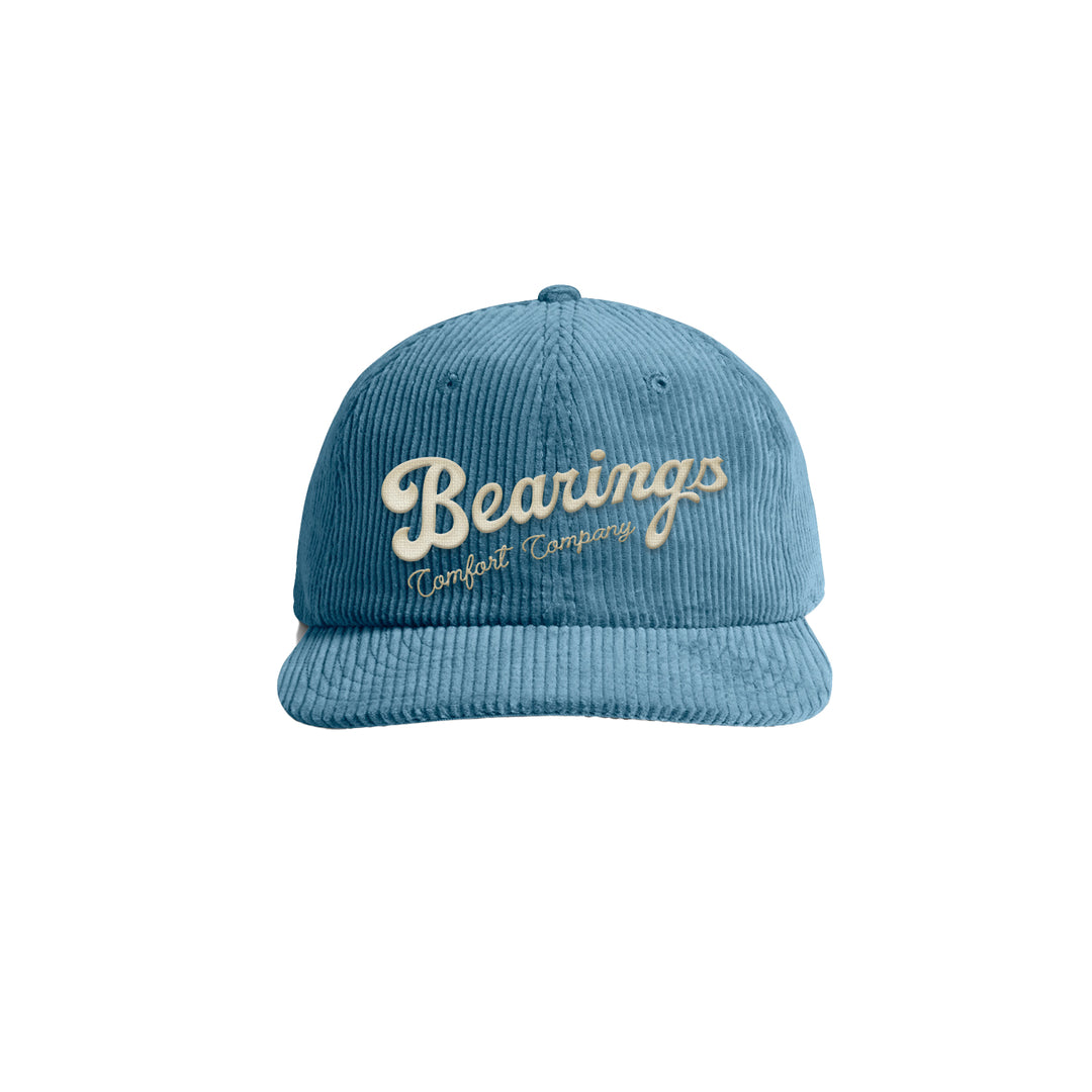 A blue corduroy Bearings Dad Hat with Bearings Comfort Company embroidered on the front in cream and yellow, shown on a white background.