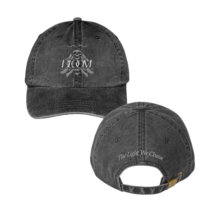 A black, distressed Bloom Dad Hat shown front and back. The front has a skull and crossbones with BLOOM. The back features The Light We Chase embroidered above the adjustable strap.