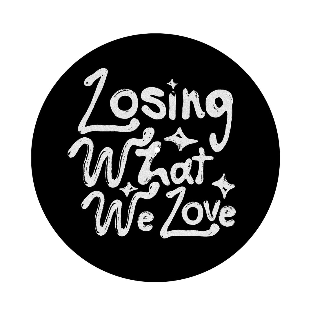 White hand-drawn text on this black Knuckle Puck slip mat reads “Losing What We Love,” accented by small decorative sparkles.