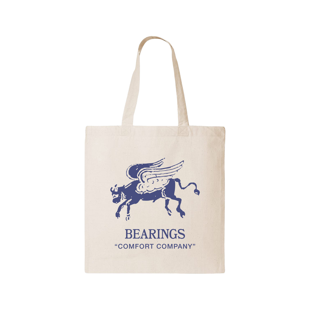 A beige Bearings tote bag with a blue Wing Bull illustration above “BEARINGS ‘COMFORT COMPANY’” printed on the front.