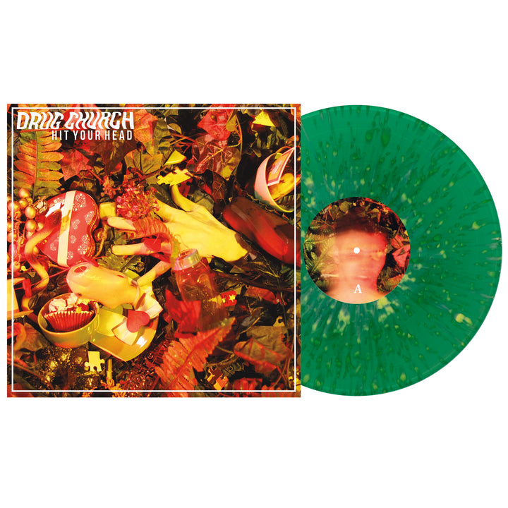 The image shows a neon yellow splatter vinyl record next to its album cover, which features yellow gloves among red and green foliage. This is the Hit Your Head vinyl from the brand Drug Church.
