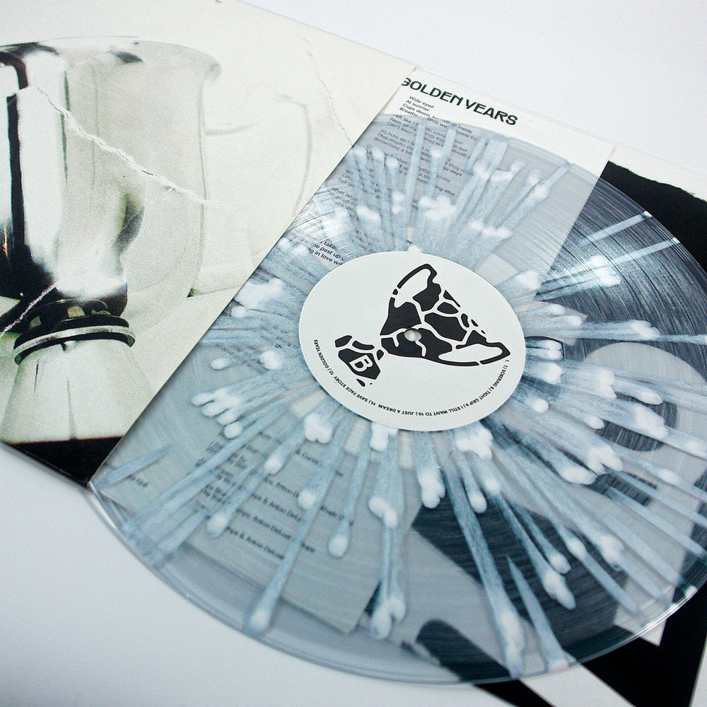 A clear white splatter vinyl record by State Champs partially slides out of its sleeve, revealing a modern abstract black and white cover with the title Golden Years.