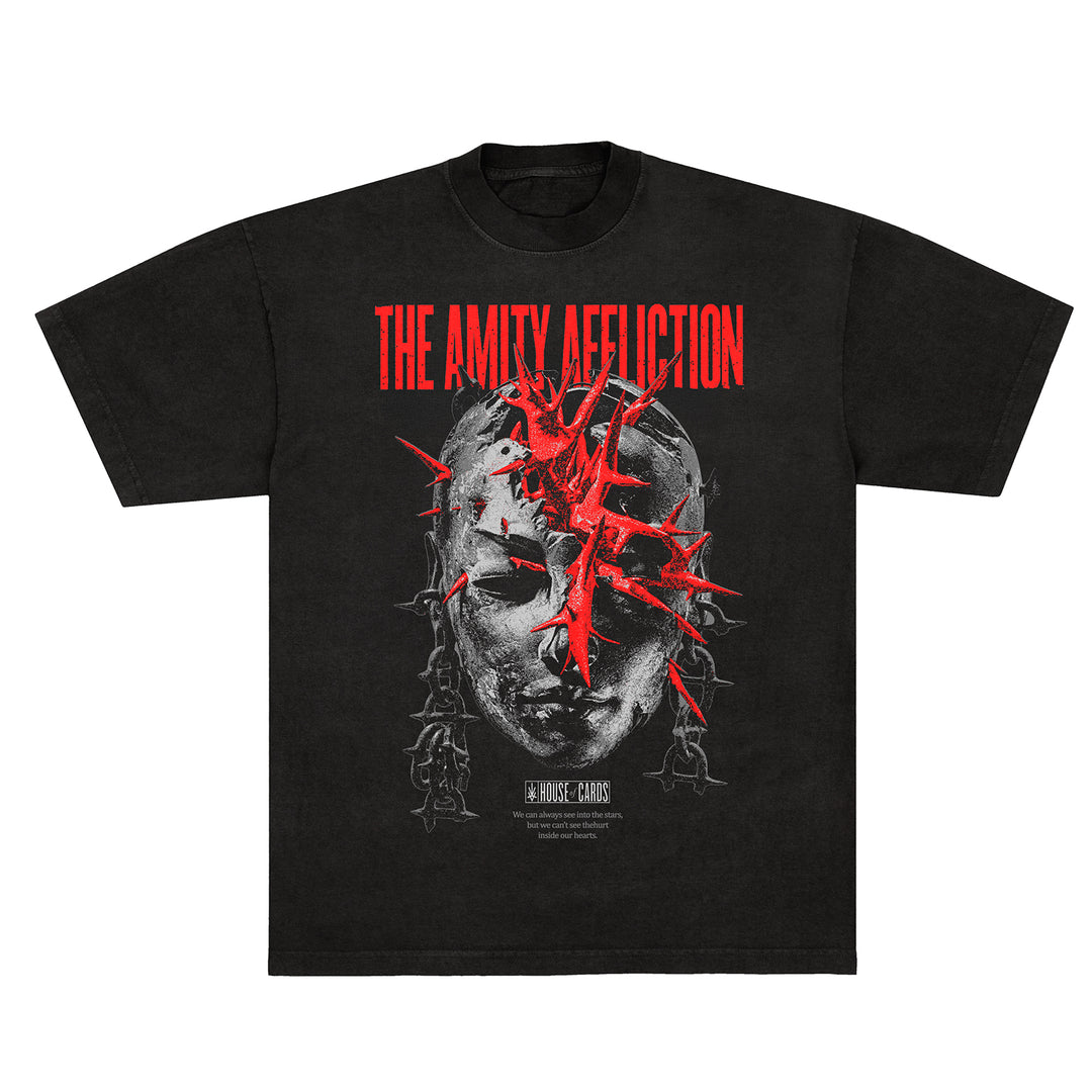 A black t-shirt by The Amity Affliction featuring a cracked stone-like face with red shards and “THE AMITY AFFLICTION” in red above, “BEYOND THE CHAOS” in white below, plus smaller custom apparel text.