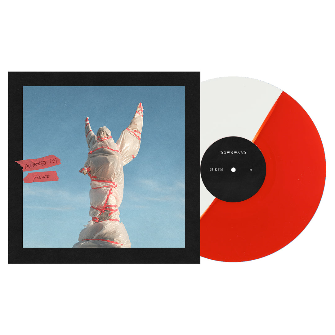 A Half White/Half Red vinyl record by DOWNWARD sits by its album cover, showing a statue wrapped in plastic and tape against a blue sky. The cover is labeled "DOWNWARD (2xLP) Deluxe Vinyl LP.