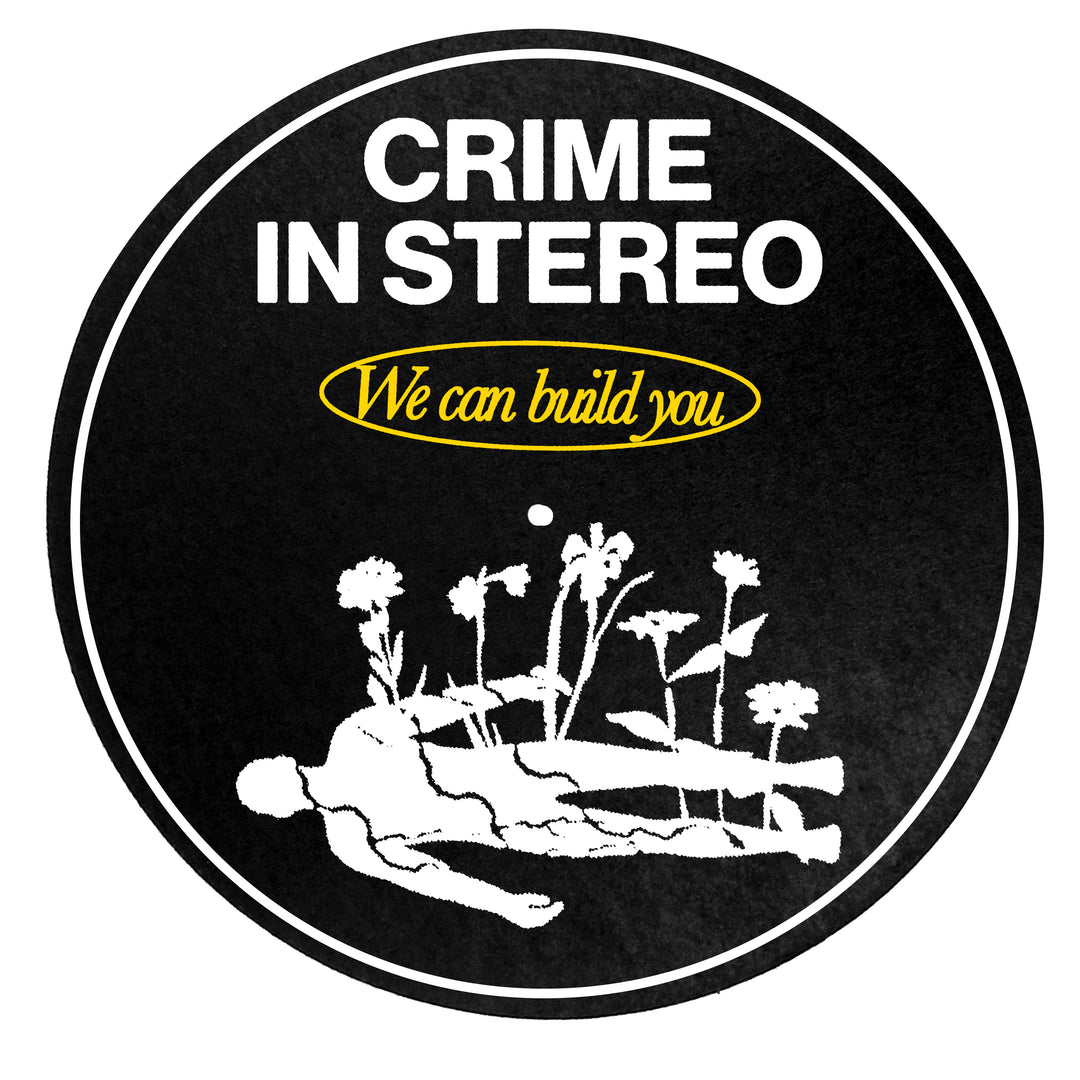 A black circular slip mat from Crime In Stereo featuring their logo, We can build you in yellow at the top, and a white outline of a person lying down with flowers growing around them.