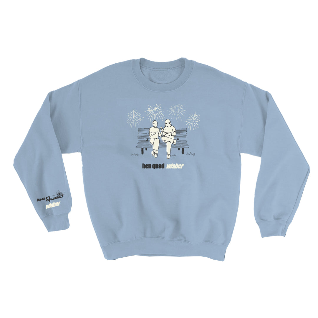 Light blue Ben Quad crewneck sweater with a line drawing of two people on a bench under fireworks. Ben quad wisher is printed below; smaller text appears on the left sleeve.
