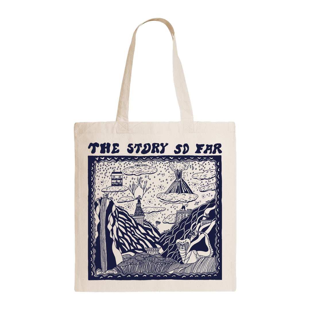 The Story So Far beige tote bag featuring dark blue illustrated mountains, trees, clouds, and figures, with THE STORY SO FAR in bold stylized letters at the top.