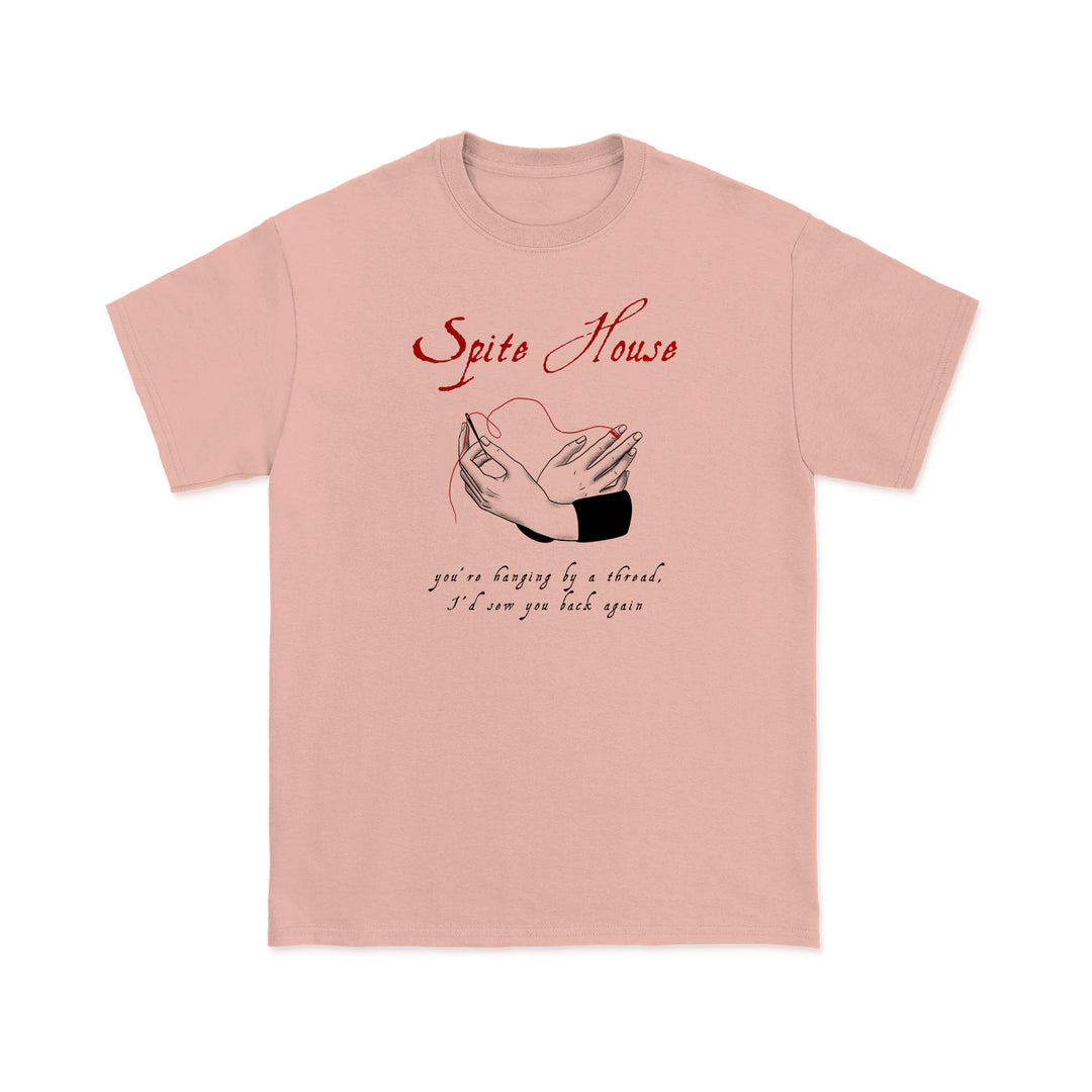 Light pink Spite House t-shirt with Spite House in red above clasped hands; black text below reads, youre happy by a thread. Ill sew you back you.