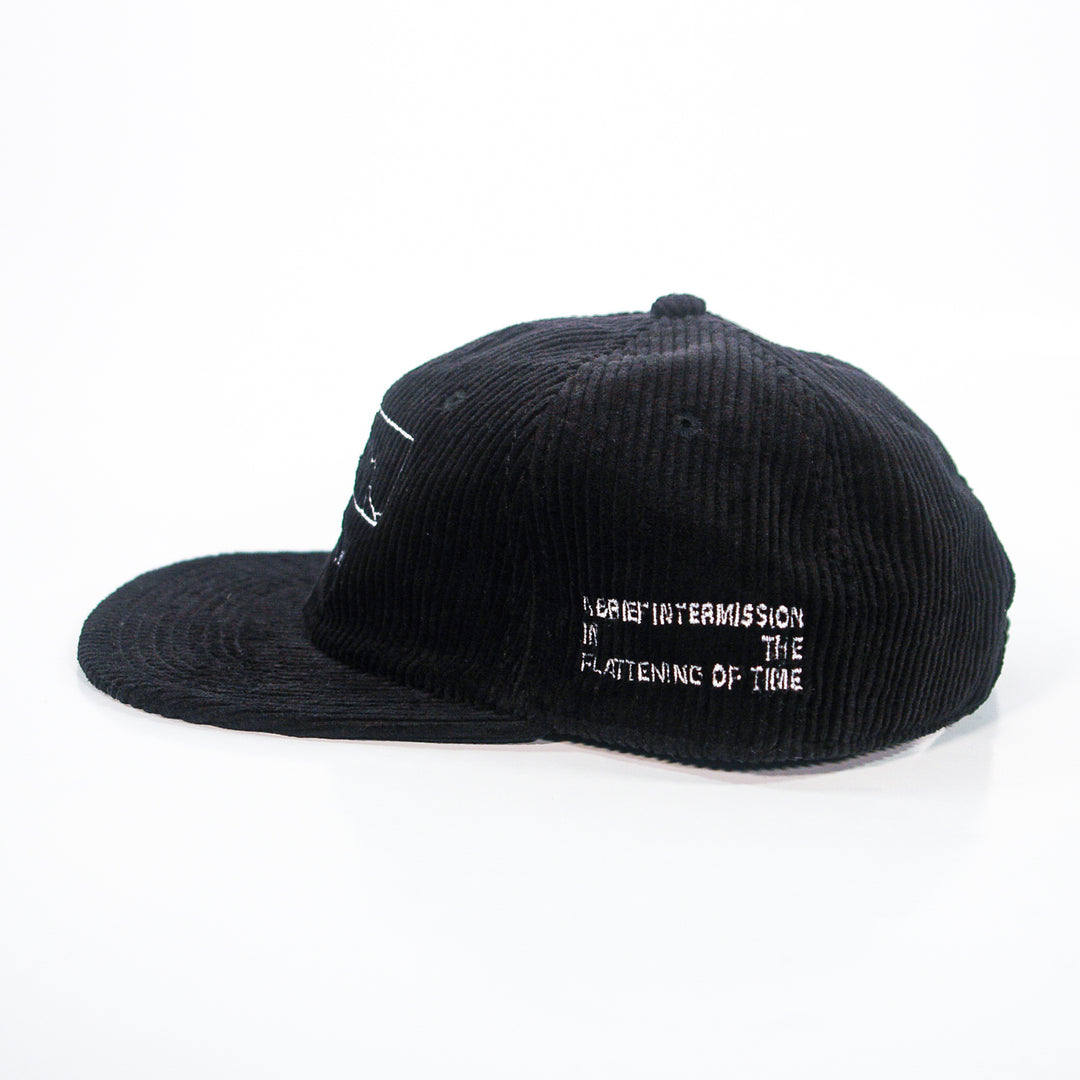 A black Spanish Love Songs AS Colour cord cap with white embroidered text on the side, "A SHORT INTERMISSION IN THE FLATTENING OF TIME," photographed on a white background.