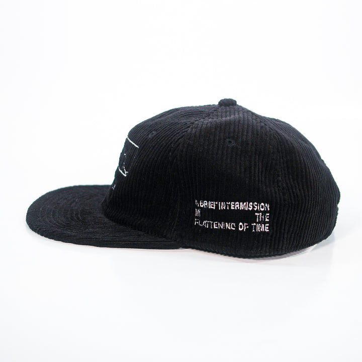 A black Spanish Love Songs AS Colour cord cap with white embroidered text on the side, "A SHORT INTERMISSION IN THE FLATTENING OF TIME," photographed on a white background.