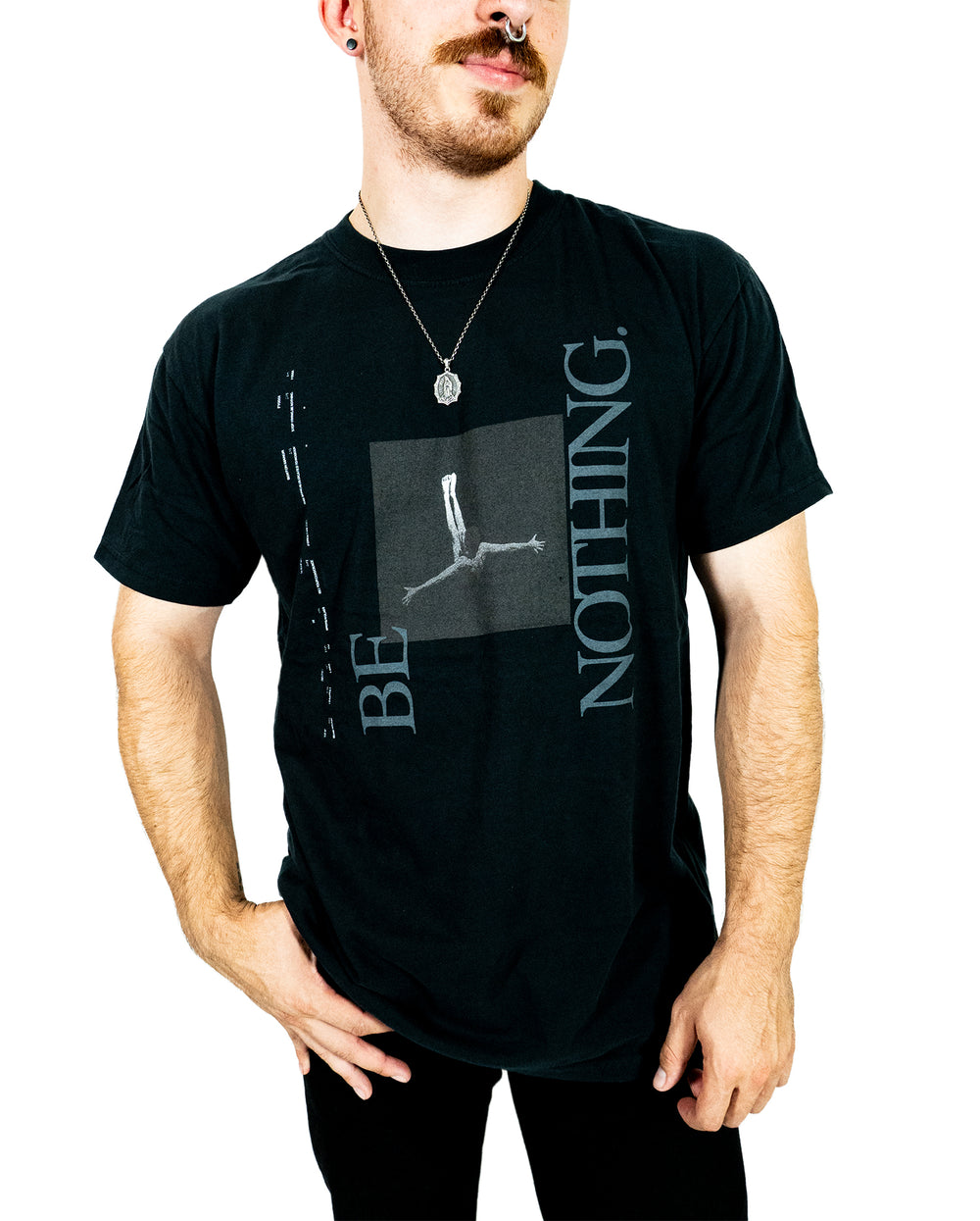 Person wearing a black Comfort Colors printed t-shirt featuring a graphic of a person in a horizontal pose and the words BE NOTHING. in large, stylized letters. The person also wears a pendant necklace.