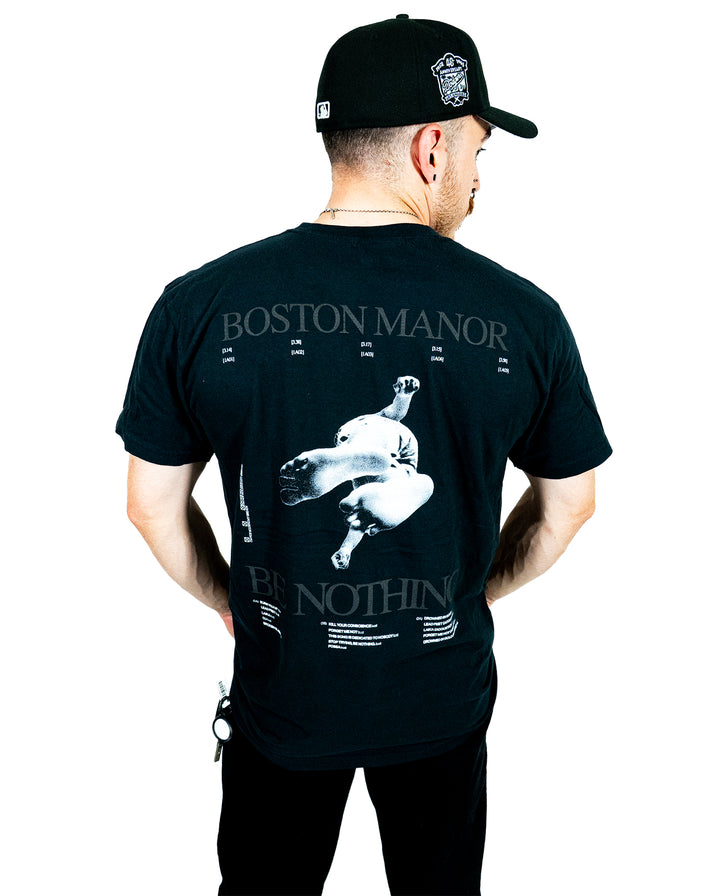 A person wearing a black cap and a black Boston Manor band t-shirt with white graphics and text printed on the back, standing and facing away from the camera, showcases the classic style of printed t-shirts.
