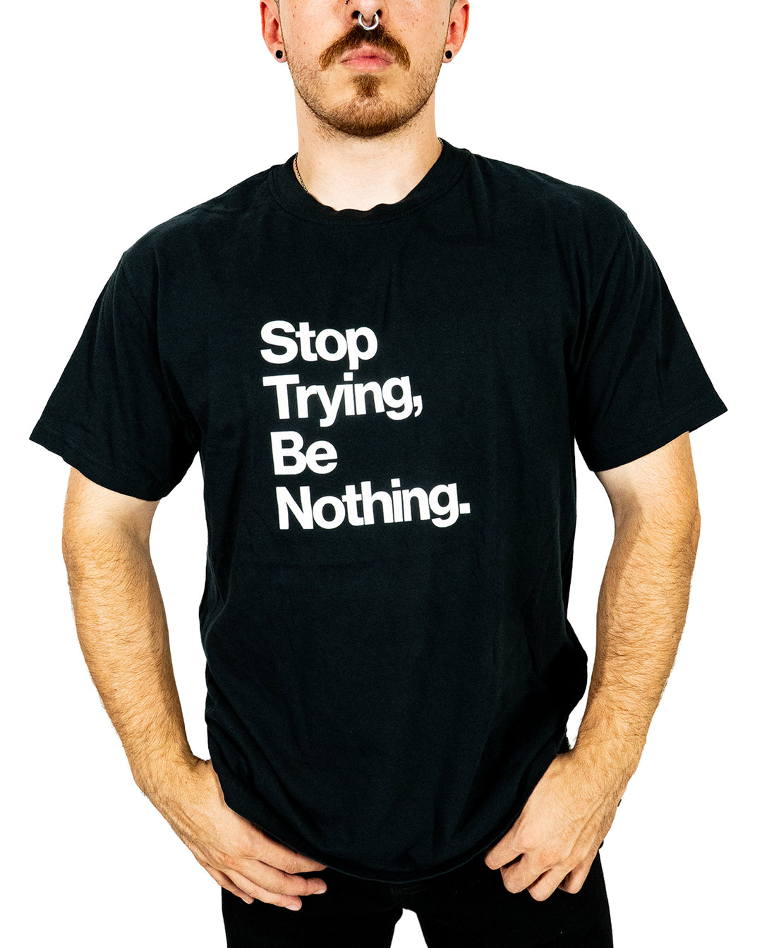 Person wearing a black Comfort Colors printed t-shirt with bold white text that reads, Stop Trying, Be Nothing. The person stands with hands at their sides, visible from mid-thigh up, on a white background.