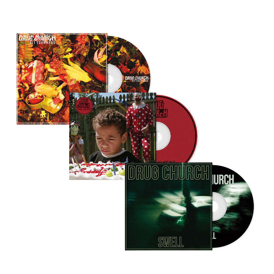 Three Drug Church CDs and their cases are shown: Hit Your Head with a chaotic, colorful cover; Cheer, showing a child and cake; and Swell, featuring a green-toned blurred image.