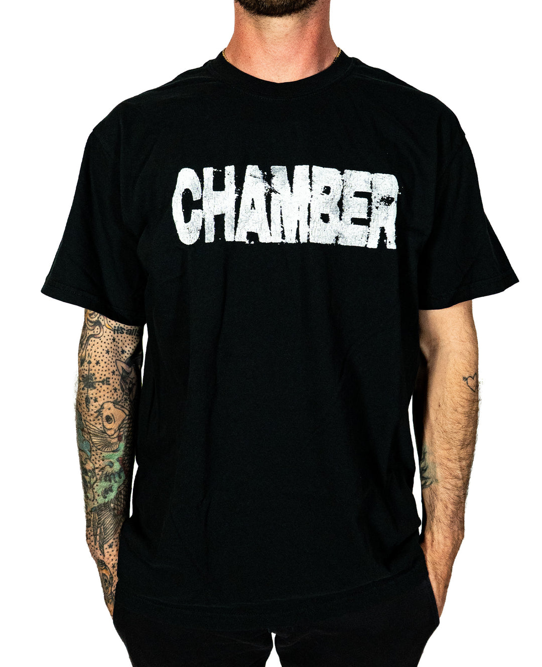 A person wearing a black Chamber t-shirt with "CHAMBER" in bold, distressed white letters across the chest stands out, their tattooed arms contrasting against a simple background.