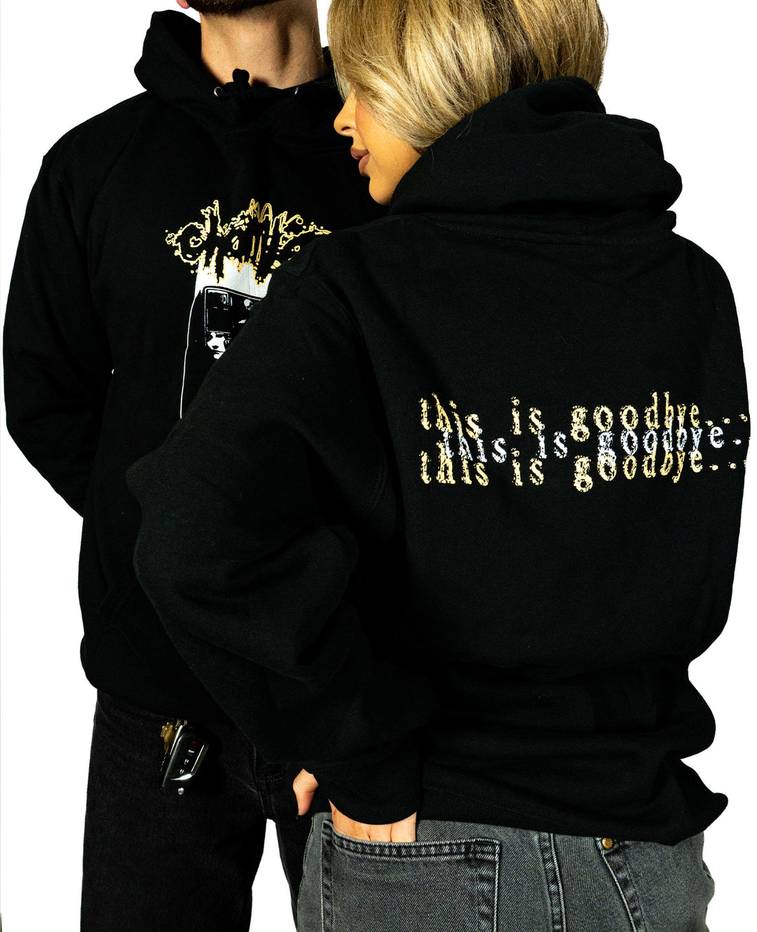 Two people in black Chamber custom apparel: the woman’s printed sweatshirt reads “this is goodbye...” in a gold, glitched font, while the man wears an abstract graphic. Both sport Chamber hoodies and face away from the camera.