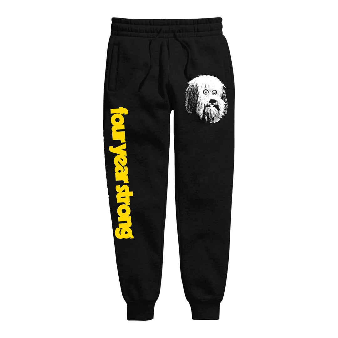 Black sweatpants by Four Year Strong feature a white dog’s face on the right hip and “four year strong” in bold yellow text running vertically down the left leg.