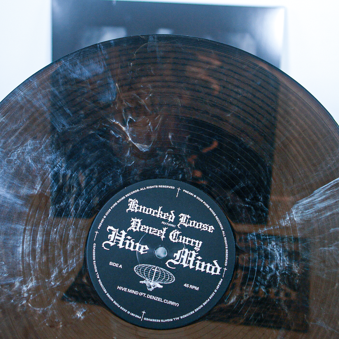 A close-up of a black and clear marbled vinyl pressing shows fingerprints and smudges. The label reads “Knocked Loose,” with track details and artist credits printed in sharp white text.