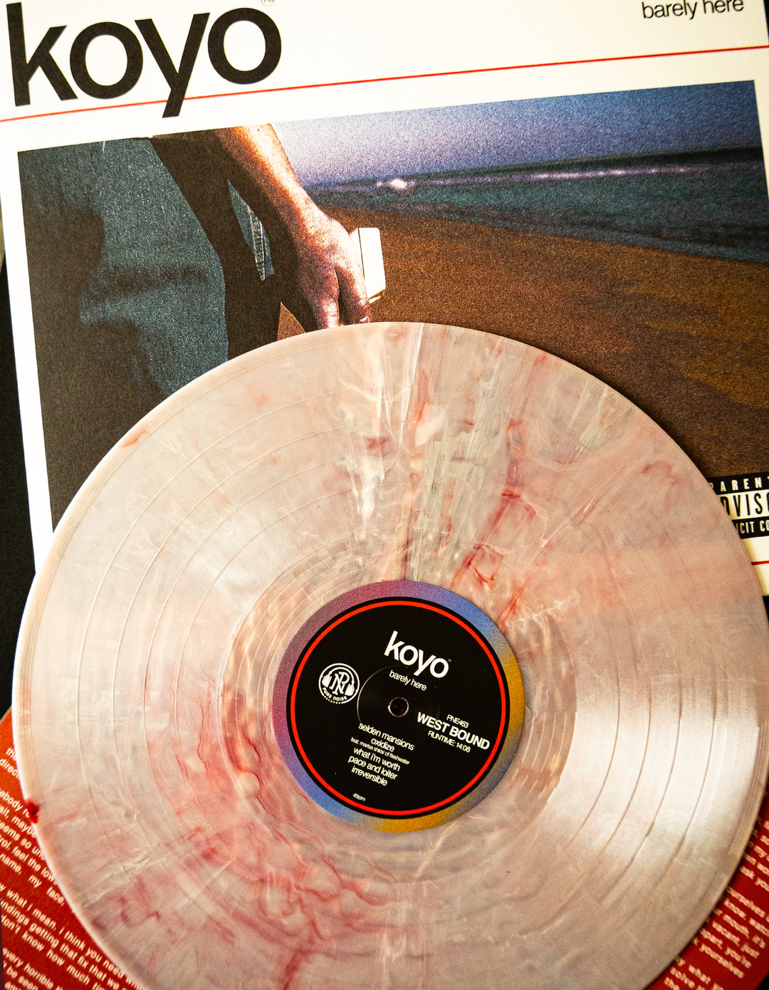 A KOYO Centurion Marble Vinyl rests on its album sleeve, which depicts a hand holding a letter by the sea at dusk. The Barely Here LP title is partially visible at the top—ideal for any vinyl presale collection.