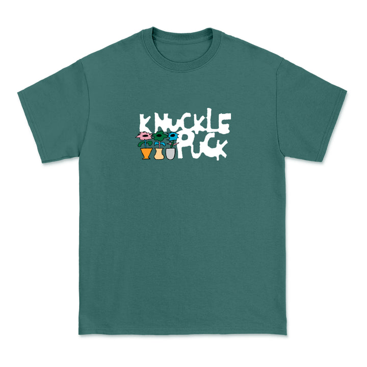 A teal Comfort Colors shirt by Knuckle Puck, printed with the band name in bold white playful letters above three colorful cartoon characters.