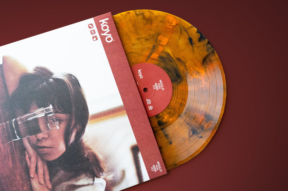 A KOYO Koi Pond Marble orange and black vinyl record slides out of its sleeve, which displays a soft-focus photo of a person resting their head on their hand while holding a glass up to their face.