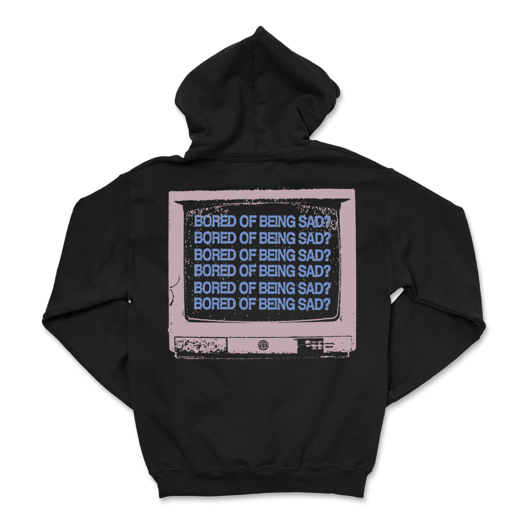 A black printed hoodie from Microwave features a graphic of an old TV screen on the back with repeated blue "BORED OF BEING SAD?" text on a pink background—perfect for custom apparel enthusiasts.