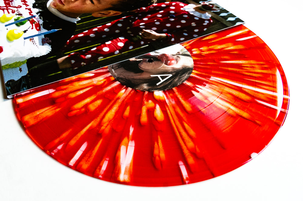 A limited edition Drug Church red and orange marbled vinyl record, partially pulled from its sleeve featuring a photo of a child at a birthday party with cake and polka-dot decorations.