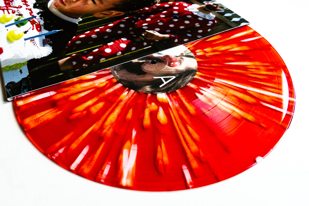 A limited edition Drug Church red and orange marbled vinyl record, partially pulled from its sleeve featuring a photo of a child at a birthday party with cake and polka-dot decorations.