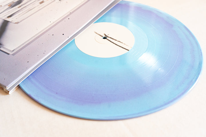 A close-up of a Spite House Desertion Violet & Baby Blue glitter vinyl LP, partially pulled from its cover on a white surface. Translucent record; album releases September 16th, 2025.