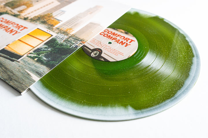 A translucent green Bearings vinyl partially pulled from its sleeve, featuring a city and a yellow moving truck labeled COMFORT COMPANY. The matching label makes this presale release a must-have for collectors.