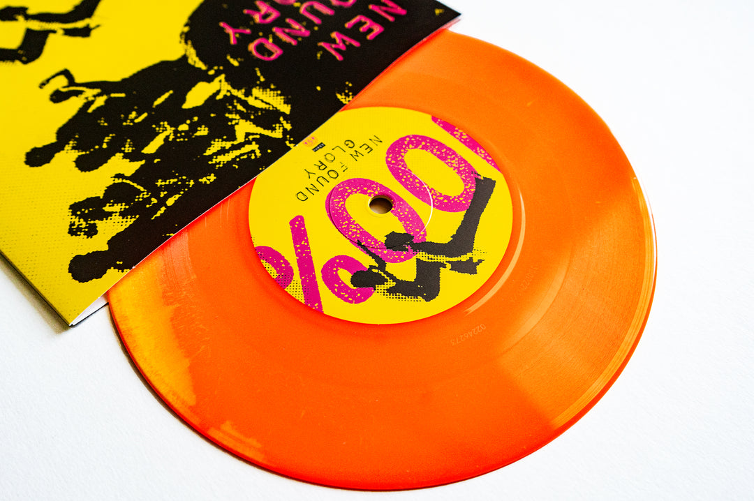A translucent orange vinyl record by New Found Glory, partially out of a neon yellow and black sleeve with bold neon pink text and graphics, lies on a white surface.