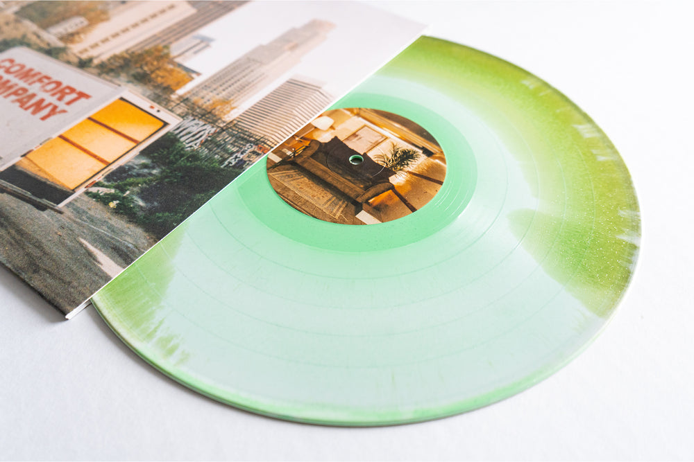 A Bearings translucent green glitter vinyl LP peeks from its sleeve featuring an urban cityscape with buildings and a yellow trailer; the label displays a cozy living room—an eye-catching pick for any album presale.