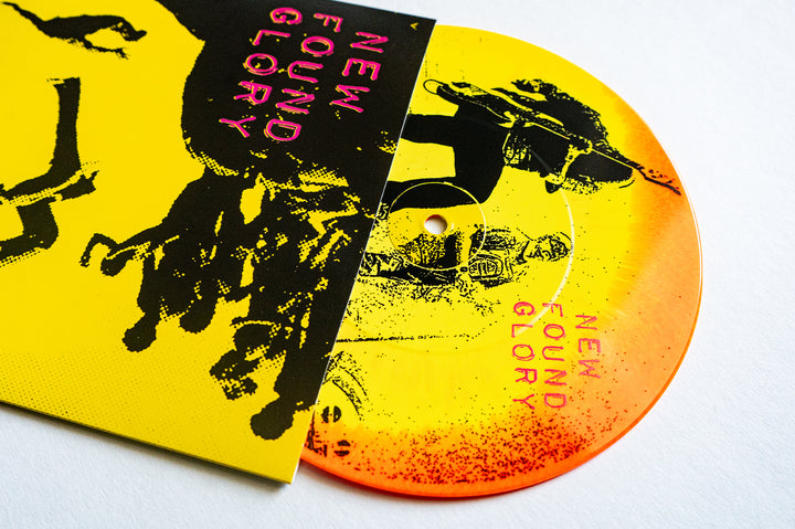 A neon yellow/orange splatter vinyl record from New Found Glory is partially inside a matching yellow sleeve, both displaying black and neon pink New Found Glory text with bold black graphic imagery.