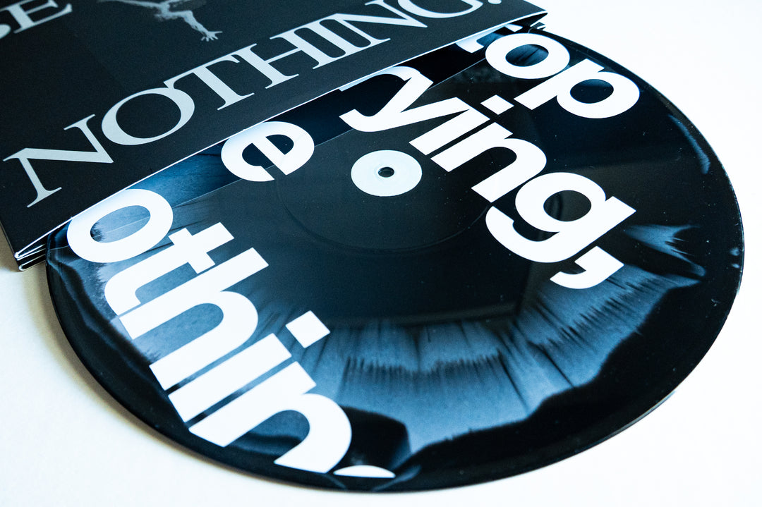 A close-up of a black vinyl record partially in its sleeve, featuring bold white text wrapping around the record and cover. This special Vinyl Pressing from Boston Manor celebrates the 10 Year Album anniversary of Be Nothing, making it a must-have for collectors and fans alike.